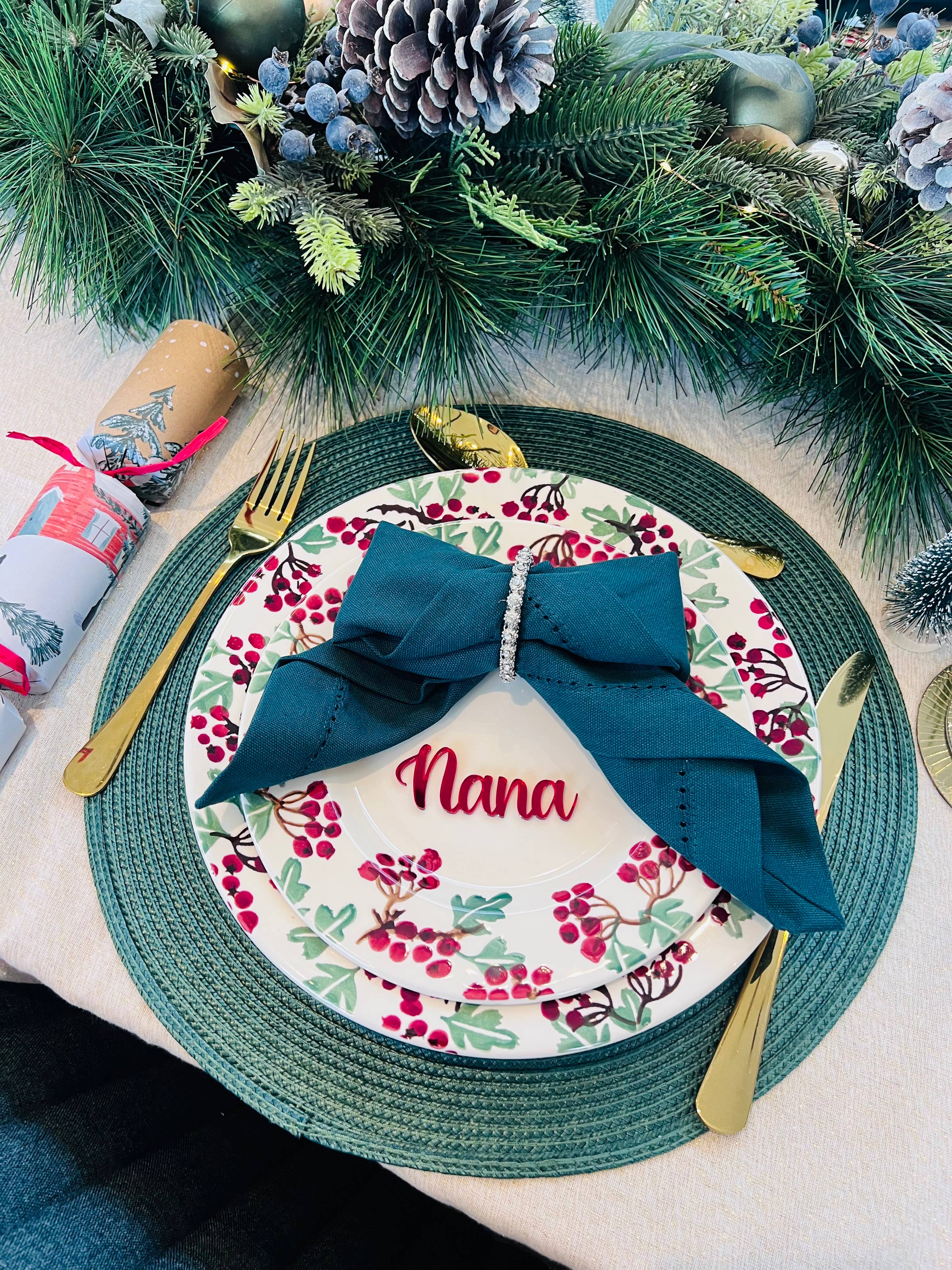 Christmas dinner table setting with personalised acrylic place name ‘Nana’ in red, festive plate and green napkin